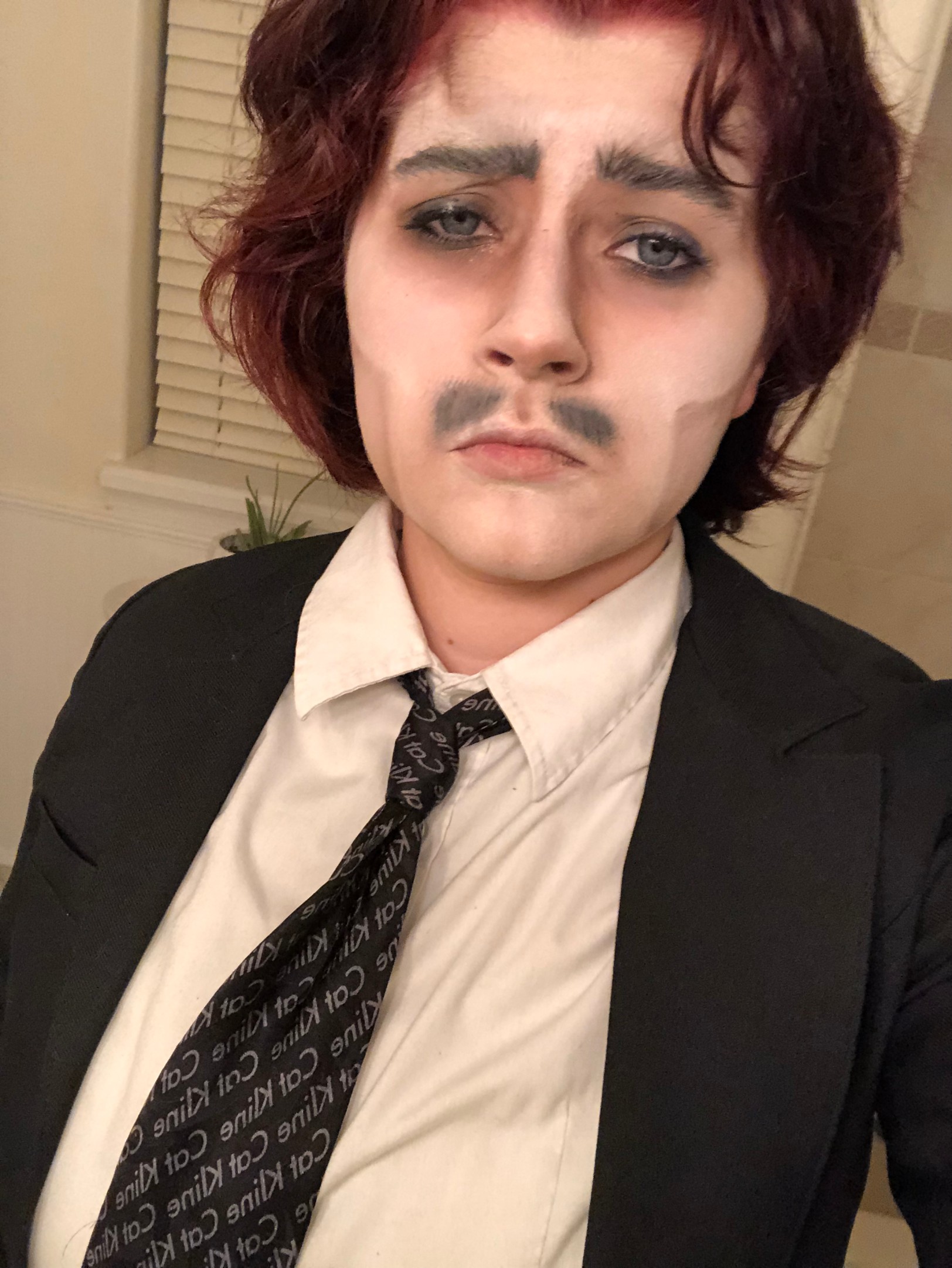 a drag king in a suit with chin length reddish hair and thick black eyebrows and mustache gazes handsomely