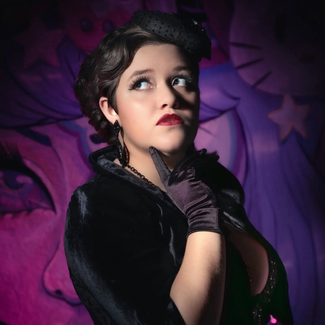 Pale person with makeup dressed in black in front of a purple background